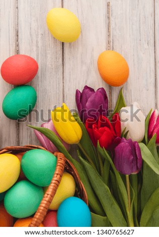 Colorful easter eggs, spring tulips on wooden texture background. On a white wood table, colored eggs, colors flowers. Happy religious day, traditional for people. Top view. Copy space.