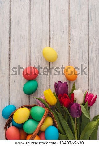 Colorful easter eggs, spring tulips on wooden texture background. On a white wood table, colored eggs, colors flowers. Happy religious day, traditional for people. Top view. Copy space.