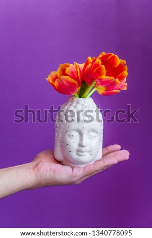 Buddha head with gred tulips in man's hand  buds  on a vibrant violet background, yoga zen meditation concept