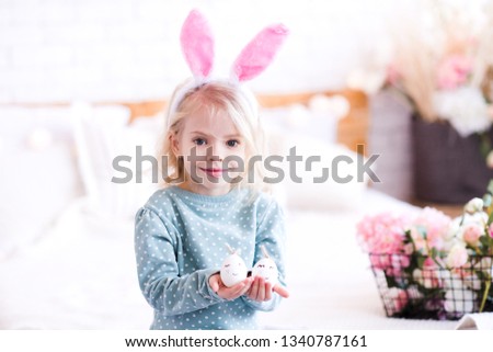 Smiling kid girl 3-4 year old holding Easter eggs and wearing rabbit ears closeup. Looking at camera. 