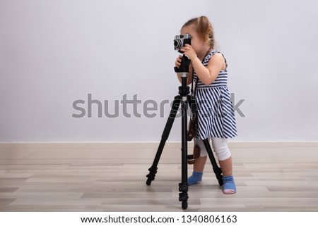 Small Innocent Girl Standing On Floor Taking Photo With Camera And Tripod