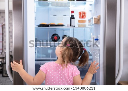 Rear View Of Girl Standing In Kitchen Opening Fridge Door Looking Inside