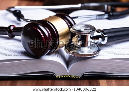 Close-up Of Stethoscope And Mallet Over Opened Law Book On Wooden Desk Royalty-Free Stock Photo #1340806322