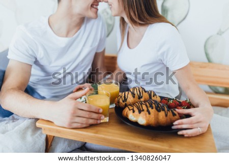 Young beautiful couple have breakfast in the morning on their bed. Croissants on the tray. Close-up picture.