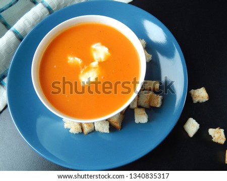 
Pumpkin cream soup on a blue plate with cream cheese and croutons on a black background