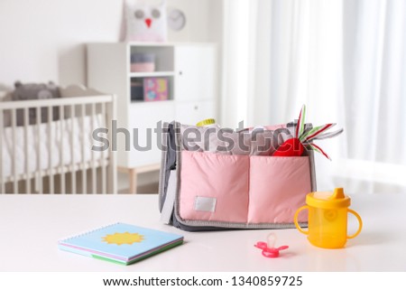 Maternity bag with baby accessories on table indoors. Space for text Royalty-Free Stock Photo #1340859725