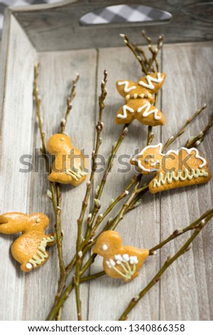Fresh baked and painted Easter gingerbreads on gray wooden tray and fresh tree branches, animals shapes, traditional Easter edible still life