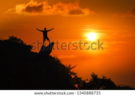 Man standing on the top of the mountain looking at red sky sunset background. 