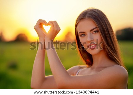 Woman showing heart on nature. Girl gesturing heart shaped hands smiling happy and loving. Pretty joyful  girl gesturing heart shaped over sunset background. 