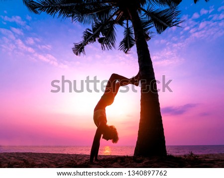 Beautiful young woman practices yoga at the beach. Early morning exercise. Sunrise. Palms background