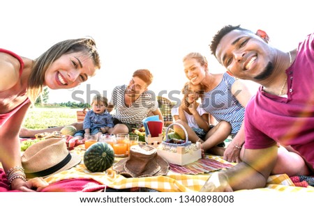 Happy multiracial families taking selfie at pic nic garden party - Multicultural joy and love concept with mixed race people having fun together at sunset picnic barbecue - Warm vivid sunshine filter