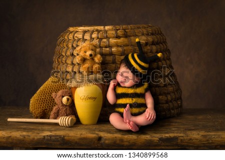 Sleepy cute baby in bee outfit resting against an antique beehive