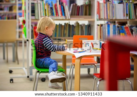 Smart todller boy, educating himself in a library, reading books and looking at pictures