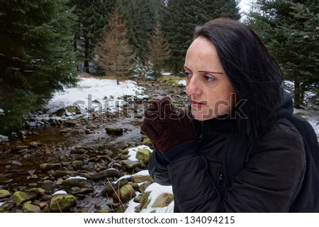 woman looking concerned / cold by stream in snow covered forest in winter