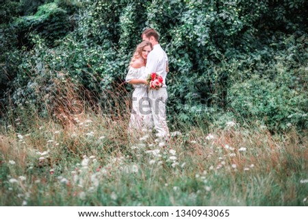 Bride and groom with a bouquet of peonies posing against the backdrop of the forest