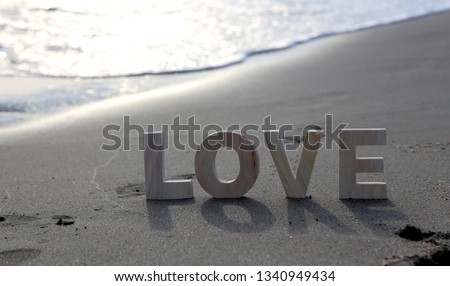 Word "Love" spelled out in wooden print letters at beach in sand with backlight and waves rushing in