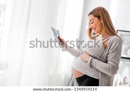 Pregnant woman at home looking her baby on ultrasound image, usg photo