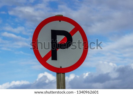 close up of a round red and white no parking sign on a wooden pole with clouds