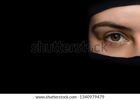 Close-up portrait of muslim woman eyes wearing the face hijab, isolated on black background with copyspace