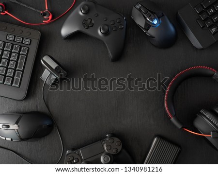 gamer workspace concept, top view a gaming gear, mouse, keyboard, joystick, headset, mobile joystick, in ear headphone and mouse pad on black table background with copy space.