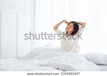 Asian woman wake up in the morning, sitting on white bed and stretching, feeling happy and fresh Royalty-Free Stock Photo #1341003347