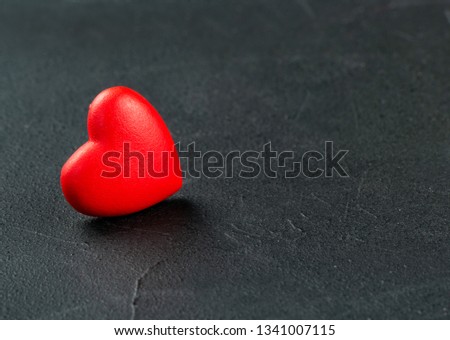 One red plastic heart on a dark concrete background