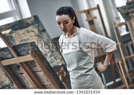 A young beautiful woman is a painting artist while working in a studio