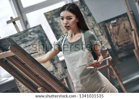 A young beautiful woman is a painting artist while working in a studio