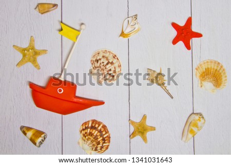 Concept of travel - toy boat,various exotic shells and other sea treasures on a light wooden background with sand view from the top.