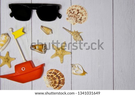 Concept of travel - toy boat, hat, sunglasses various exotic shells and other sea treasures on a light wooden background with sand view from the top.