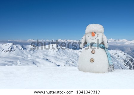 Funny plush snowman in winter landscape, mountains and snow with copy space