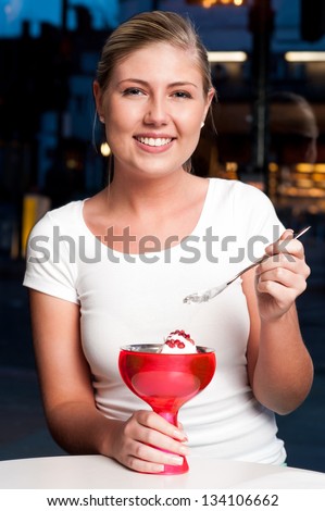Attractive beautiful young woman eating an ice cream in cafe.
