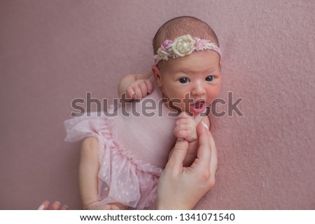 Mother holds her little newborn daughter by the hand. Girl in a pink lace dress on a pink wool blanket.