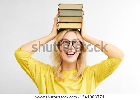 A beautiful woman in glasses is holding a stack of books above her head and is smiling toothyly on a white background. Happy and fun education