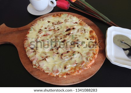 Delicious pizza with sausage and cherry tomatoes is on top view. On the table are cherry tomatoes, black olives, tomato sauce, parsley and a knife for pizza.