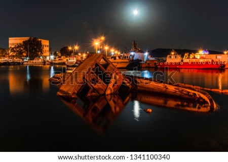 Night view of port of Elefsina with a shipwreck and full moon for background. Long exposure night picture at port of Elefsina in Attica, Greece.