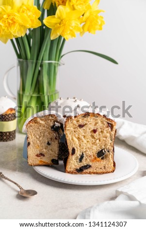 Moscow/Russia-CIRCA 03.2018: an image of Easter cakes, cut in half, inside of the cake are dry fruits, on a white plate, yellow daffodils on background, grey wall background