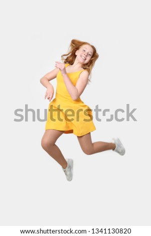 Teenage redhead girl jumping in yellow dress - full height portrait on gray background