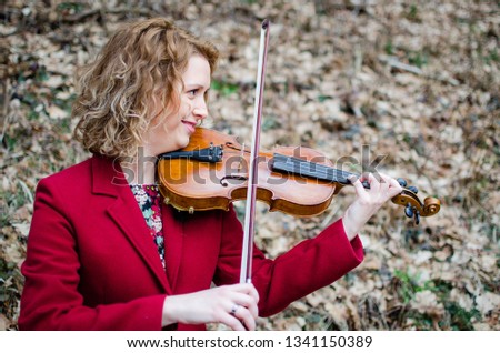blond girl  in red  keeps violin on shoulder, girl playing violin in park