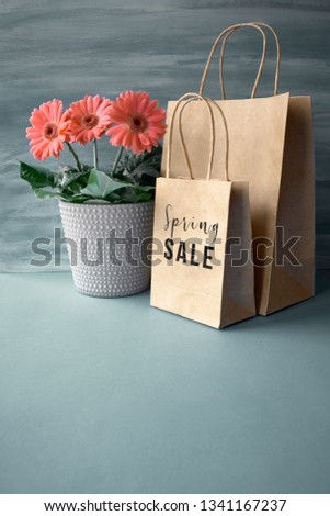 Coral gerbera daisy flowers and craft papper shopping bags on neutral background. Springtime sale concept image with text "Spring sale" on the bag, copy-space below