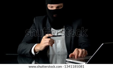 Businessman in balaclava with laptop and bank card transfers money to tax havens