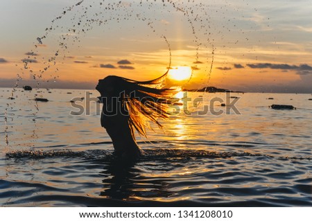 Girl in the water at sunset scatter hair. Silhouettes of girls at sea.