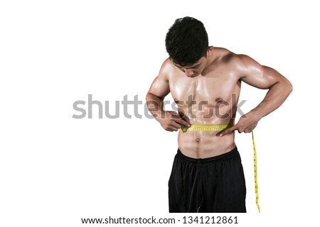 Picture of young man measuring his muscular belly while standing in the studio, isolated on white background