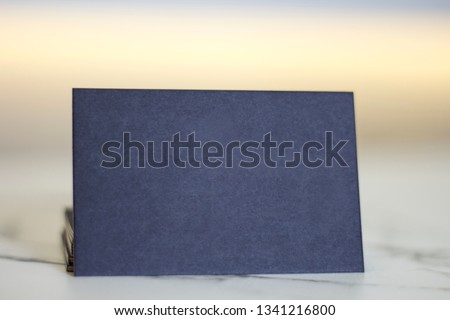Mockup of dark blue business card with texture standing on marble surface and colored background.