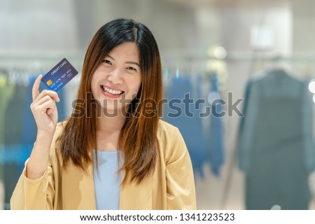 Portrait Asian woman holding and presenting the credit card for online shopping in department store over the clothes shop store background, technology money wallet and online payment concept