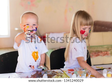 Beautiful little blonde girl and boy, has happy fun smiling face, brown eyes, white t-shirt. Painted brushes water colors in skin. Child portrait. Kids concept. Brother and sister hobby.