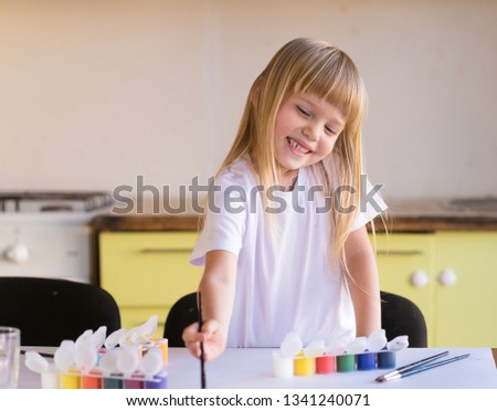 Beautiful little blonde girl, has happy fun smiling face, pretty eyes, white t-shirt. Painted brushes water colors in skin. Child portrait. Kids concept hobby.