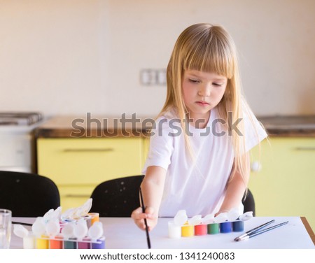 Beautiful little blonde girl, has serious sad face, pretty eyes, white t-shirt. Painted brushes water colors in skin. Child portrait. Kids concept hobby.