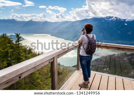 Woman Tourist Taking Photos from a Viewing Platform on the Top of a Mountain. Impressive Mountain ana Sea Scenery. Squamish, BC, Canada.