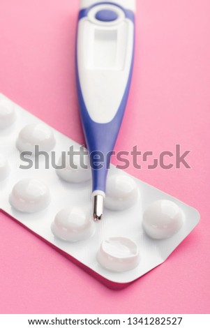 Electronic thermometer and packaging of tablets on a pink background. The concept of timely diagnosis and treatment
